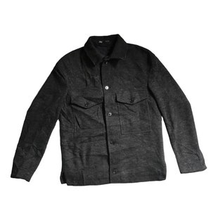 Può includere: Una giacca camicia a maniche lunghe di colore grigio scuro con chiusura a bottoni e due tasche a patta.