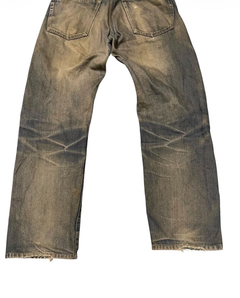 May include: Faded blue jeans with a worn appearance. The denim pants show signs of wear and tear, with visible fading and distressing throughout the fabric. The back pockets and waistband are visible.