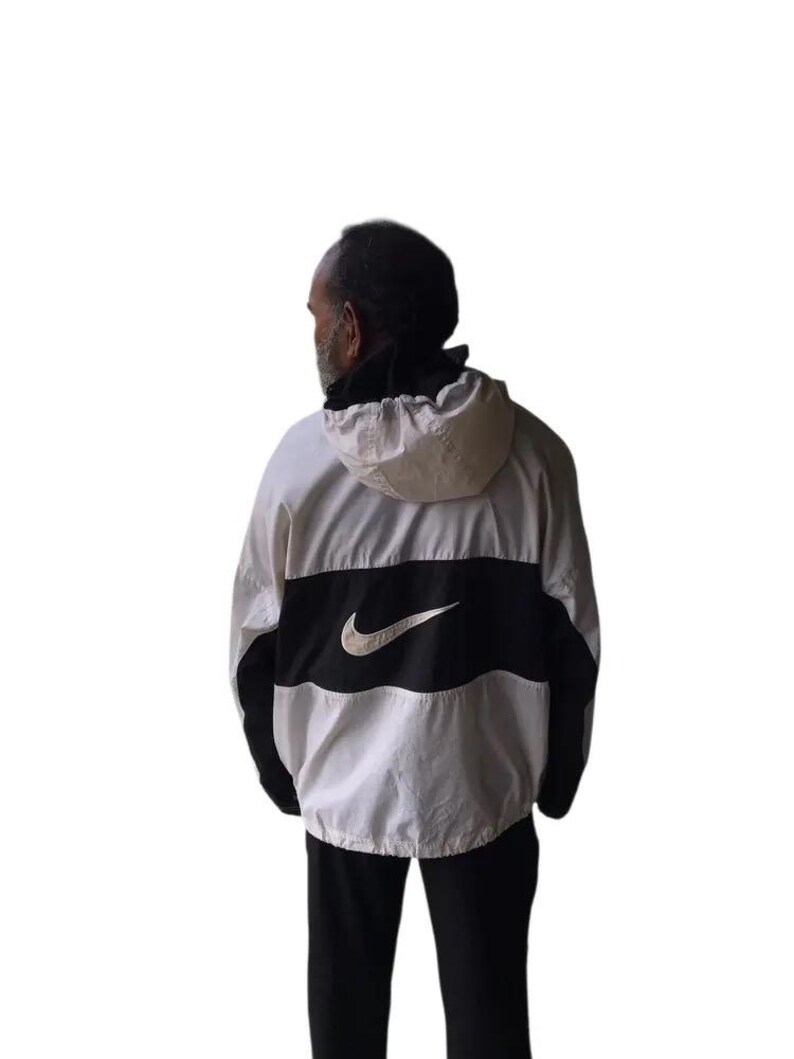 May include: White, black, and gray Nike windbreaker jacket with a hood. The jacket features a large black stripe across the chest with the Nike swoosh logo in white. The sleeves and lower portion of the jacket are black.