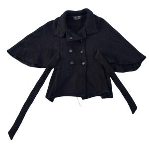 Peut inclure: Capuchon noir à manches courtes avec une fermeture à double boutonnage et une large ceinture. Le capuchon est en tissu texturé et a une silhouette légèrement évasée.