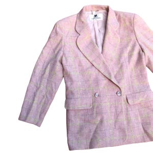 May include: A pink and white plaid blazer with a double breasted closure and a single pocket on the left side. The blazer has a label that reads "Courreges".