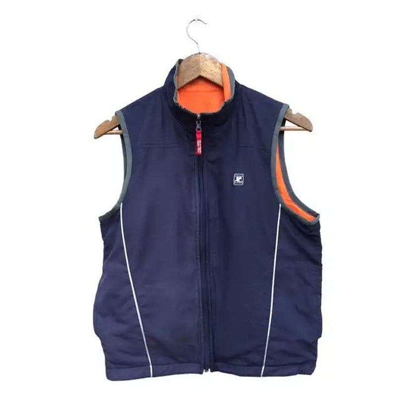 May include: A navy blue reversible vest with a zipper closure. The vest has a white stripe down each side and a small logo on the front. The vest is lined with orange fleece.