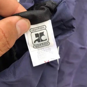 May include: A navy blue jacket with a white zipper and a white label that says "Courr&egrave;ges sport futur" with a logo of a stylized "C".