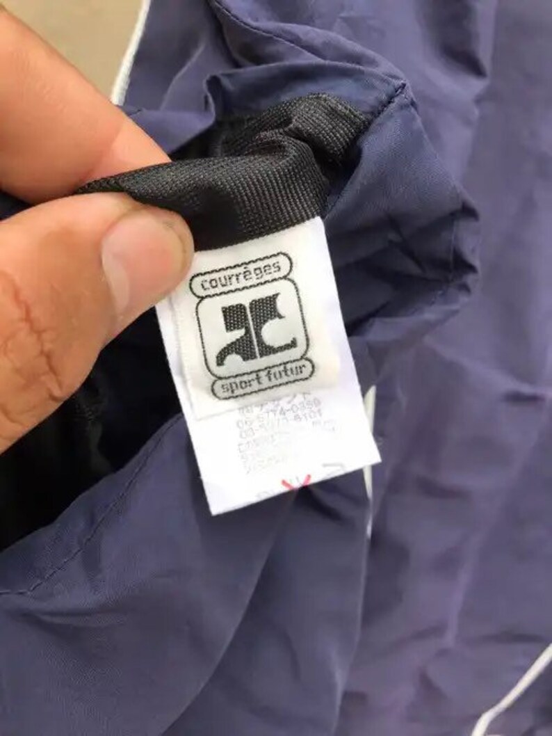 May include: A navy blue jacket with a white zipper and a white label that says "Courr&egrave;ges sport futur" with a logo of a stylized "C".