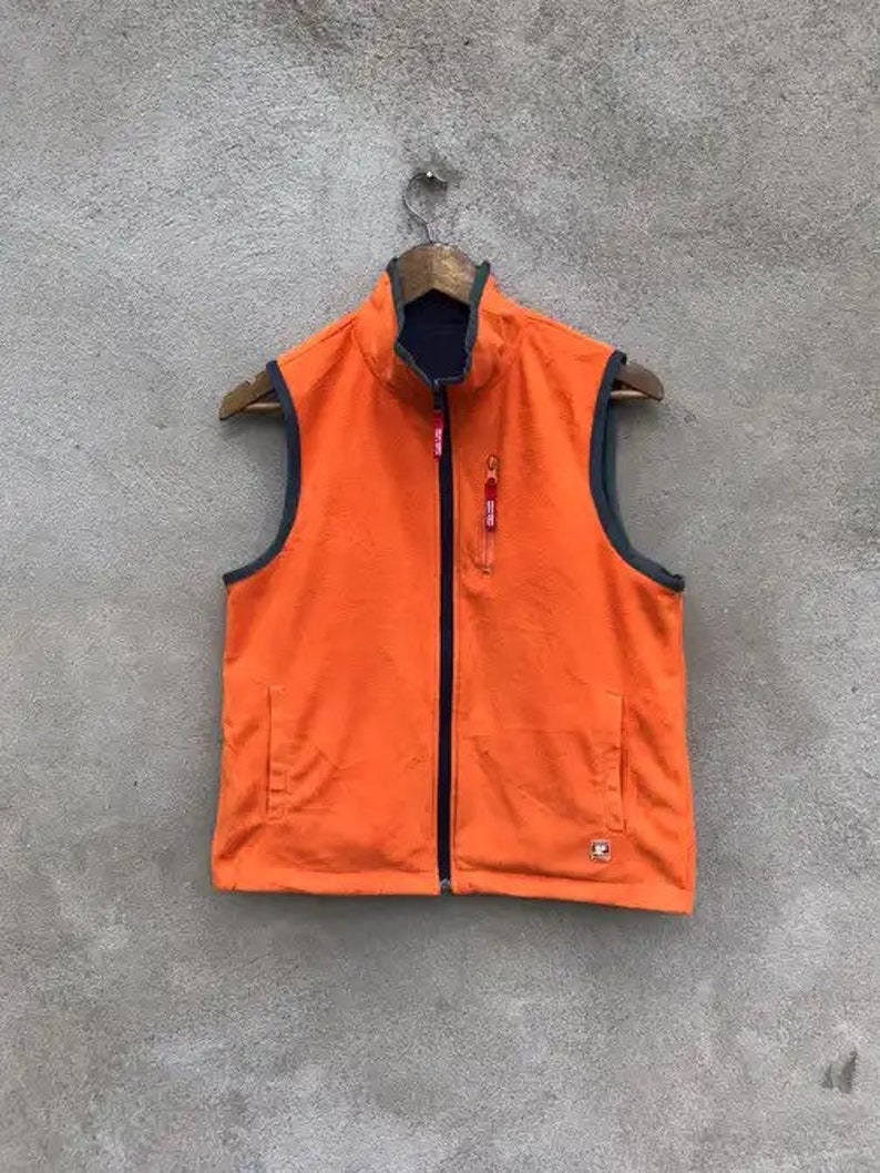 May include: Orange fleece vest with a zipper closure and a black lining. The vest has two zippered pockets on the front.