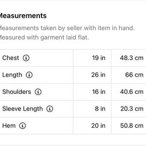 Op de afbeelding: Een tabel met de afmetingen in inches en centimeters voor de borst, lengte, schouders, mouwlengte en zoom.