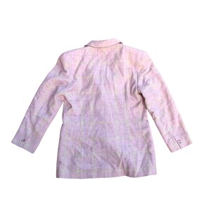 May include: A pink blazer with a subtle checkered pattern. The blazer has a classic design with long sleeves and a button-up front.