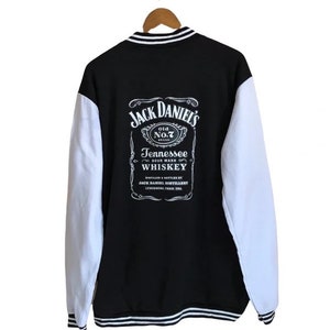 Puede incluir: Chaqueta de béisbol negra y blanca con un logotipo de Jack Daniel's en la espalda. El logotipo presenta el texto "Jack Daniel's" y "Tennessee Sour Mash Whiskey".