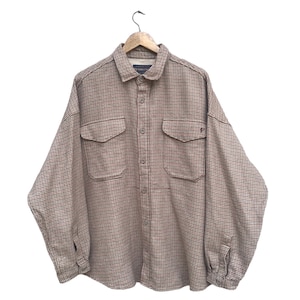 May include: A brown and beige plaid flannel shirt with a button-up front and two chest pockets. The shirt is hanging on a wooden hanger.