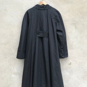 K&ouml;nnte beinhalten: Ein schwarzer Langarmmantel mit Stehkragen und Knopfleiste. Der Mantel hat eine lockere Passform und einen flie&szlig;enden Rock.