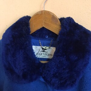 May include: A blue coat with a faux fur collar. The coat has a button closure and a label that reads "Courr&egrave;ges Paris".