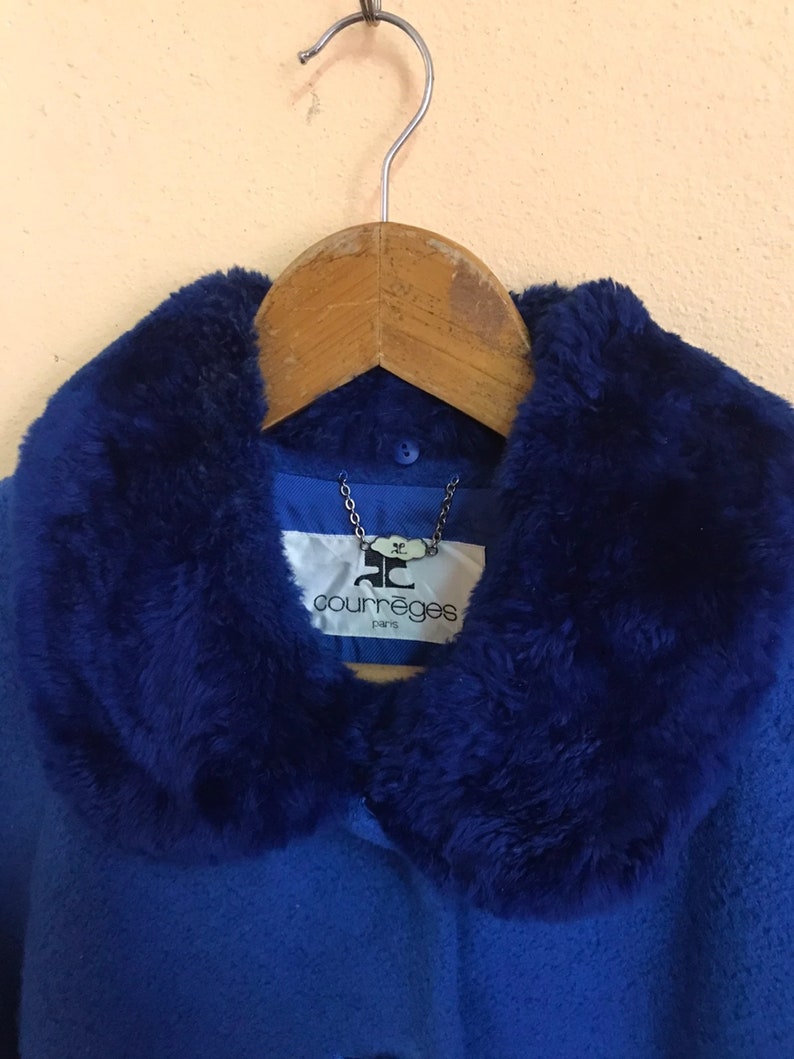 May include: A blue coat with a faux fur collar. The coat has a button closure and a label that reads "Courr&egrave;ges Paris".