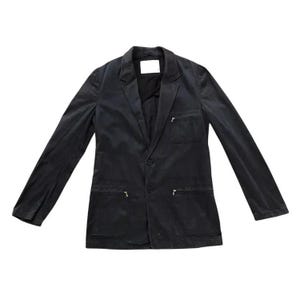 Pode incluir: Um blazer preto com lapela entalhada, dois bolsos frontais e dois bolsos inferiores. O blazer tem um fecho de um botão e mangas compridas. Uma pequena etiqueta branca é visível na parte de trás da gola.