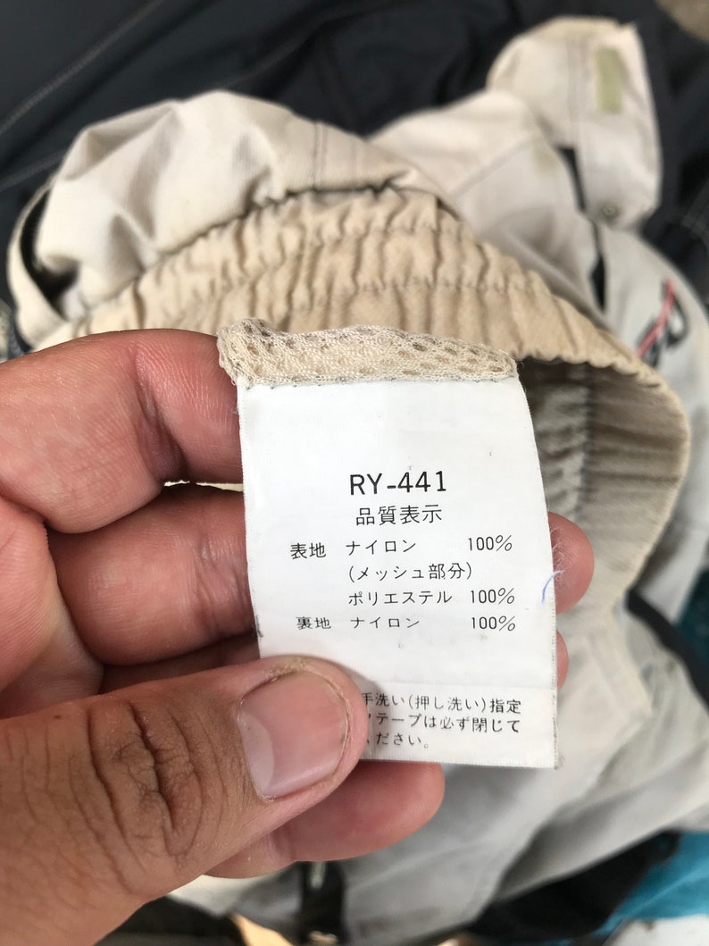 K&ouml;nnte beinhalten: Ein wei&szlig;es Etikett mit schwarzem Text, auf dem "RY-441" und "品質表示" (Qualit&auml;tsanzeige) steht. Das Etikett listet die Stoffzusammensetzung des Kleidungsst&uuml;cks auf: Nylon 100 % (Mesh-Teil), Polyester 100 %, Nylon 100 %. Das Etikett enth&auml;lt auch Waschanweisungen: "Handw&auml;sche (Pressw&auml;sche) vorgeschrieben. Klebeband muss geschlossen sein."