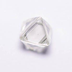 Peut inclure: Un diamant clair et non taillé, de forme géométrique. Le diamant est transparent, permettant à la lumière de traverser ses facettes. L'image est un gros plan, soulignant la clarté et la forme du diamant. Le diamant est posé sur un fond blanc.
