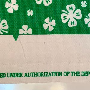 May include: Green and white fabric with a repeating pattern of four-leaf clovers, each with the letters "H" inside. The text "PROTECTED UNDER 18 U.S.C. 707; PRODUCED UNDER AUTHORIZATION OF THE DEPT. OF AGRICULTURE (USDA) FOR SPRINGS INDUSTRIES INC." is printed at the bottom.