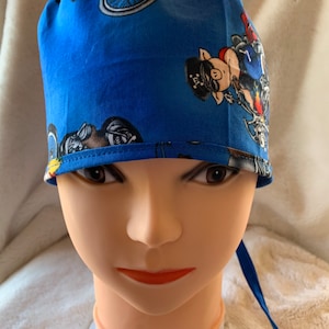 May include: Blue surgical scrub hat with a pattern of cartoon pigs riding motorcycles. The hat has a tie at the back.
