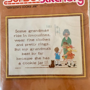 May include: A Sunset Stitchery kit titled "Grandma's Cookie Jar." The kit features a stitched design of a grandmother, two children, and a cat. The text reads, "Some grandmas ride in limousines...but my grandma's best by far because she has a cookie jar!!!"