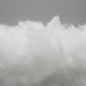 May include: A close-up of a white, fluffy material that resembles cotton. The material is soft and appears to be made of fibres.
