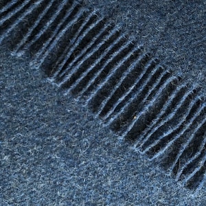 May include: A close-up of a dark blue fabric with a fringe edge. The fabric has a soft, fuzzy texture.
