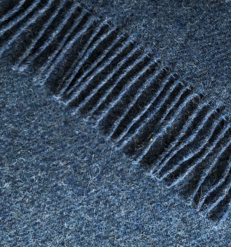 May include: A close-up of a dark blue fabric with a fringe edge. The fabric has a soft, fuzzy texture.