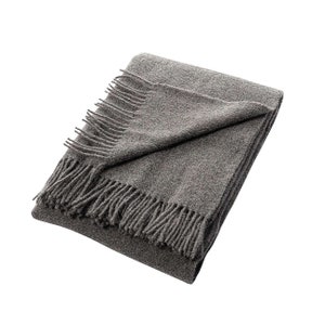 May include: A gray throw blanket with a fringed edge. The blanket is folded in half and the fringe is visible on both sides.