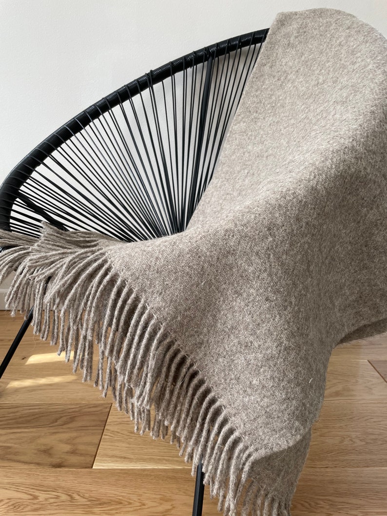 May include: A light brown throw blanket with fringe on all sides draped over a black wire chair. The blanket is made of a soft, fuzzy material.