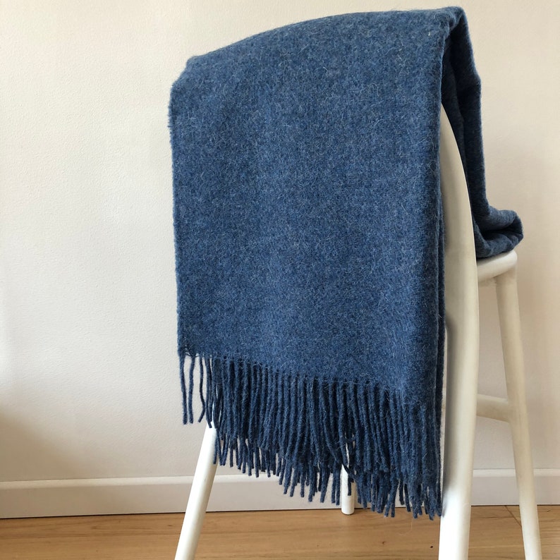 May include: A blue throw blanket with a fringe border. The blanket is draped over a white chair.