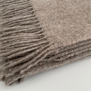 May include: A brown wool throw blanket with a fringe border. The blanket is folded in thirds and the fringe is visible on the top and bottom edges.