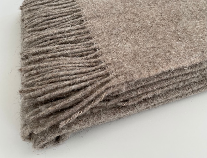 May include: A brown wool throw blanket with a fringe border. The blanket is folded in thirds and the fringe is visible on the top and bottom edges.
