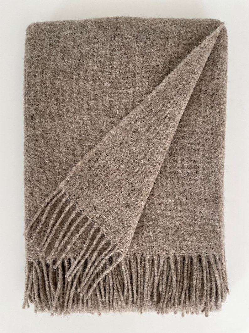 May include: A brown wool throw blanket with fringe on all sides. The blanket is folded in half and the fringe is visible on the bottom edge.