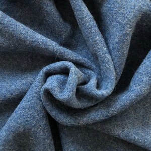 May include: Close-up of a soft, blue fabric with a fuzzy texture. The fabric is folded and draped, creating a swirling pattern.