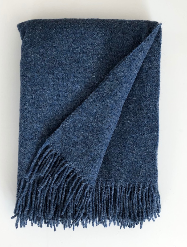 May include: A soft, blue throw blanket with a fringe border. The blanket is folded in half and has a textured surface.