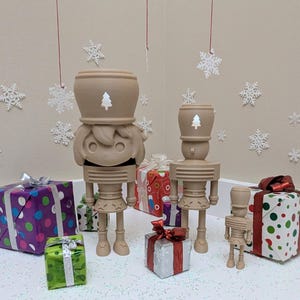 Puede incluir: Una escena festiva navideña con cuatro figuras de cascanueces de madera de varios tamaños. Cada cascanueces tiene un recorte en forma de árbol en la cabeza. Regalos coloridos envueltos con lazos están dispersos alrededor de las figuras.