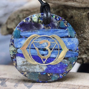 May include: Round pendant necklace with a black cord. The pendant features a blue and gold design with a gold-colored symbol in the center. The pendant is made of blue and gold stones.