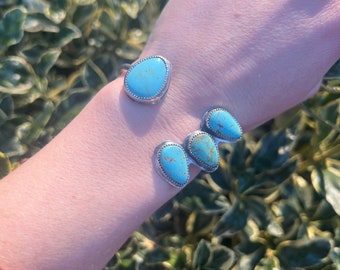 May include: A silver bracelet with three turquoise stones. The stones are oval shaped and have a light blue color with brown veins.