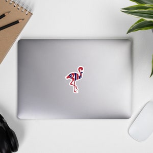 May include: A red, white, and blue flamingo sticker with a patriotic design. The flamingo is standing on one leg with its head tilted to the side.