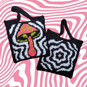 May include: Two black crochet tote bags with white and black wavy patterns. One bag features a colorful mushroom design with pink, yellow, and green accents. The other bag has a geometric design. Both bags have black handles.