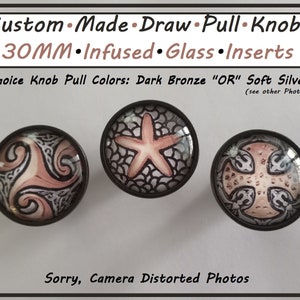 May include: Three custom-made draw pull knobs with 30mm infused glass inserts. The knobs feature various designs, including a starfish, a Celtic spiral, and a cross pattern, all in shades of peach, black, and silver. The text on the image says "Custom Made Draw Pull Knobs".