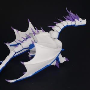 May include: A white dragon figurine with blue and purple accents. The dragon has large wings, a long tail, and sharp spikes along its back. The figurine is set against a black background.