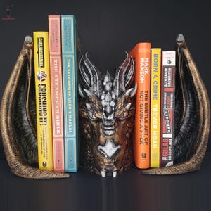 May include: A pair of dragon bookends with gold and black accents. The bookends are holding up a stack of books with titles like "The Steampunk Bible", "Born a Crime", and "The Subtle Art of Not Giving a F*ck".