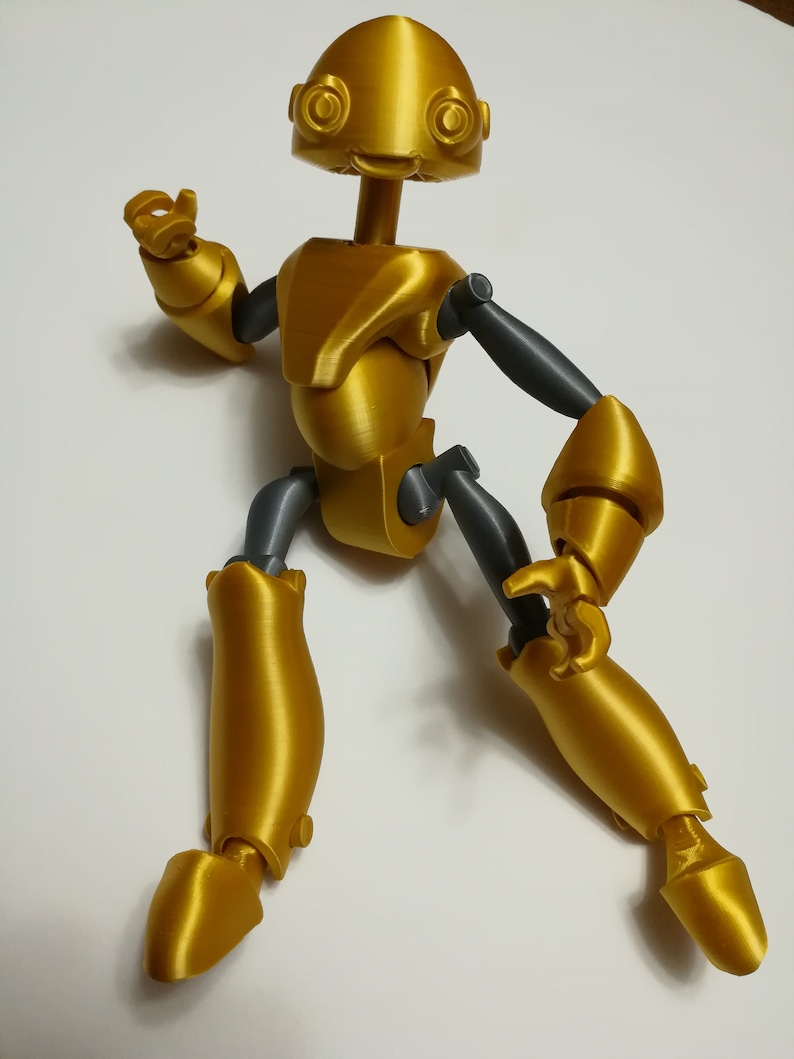 May include: A gold-colored articulated robot toy with gray joints. The robot has a large head with two large eyes and a small mouth. The robot is posed in a dynamic stance with one arm raised and the other arm bent at the elbow.