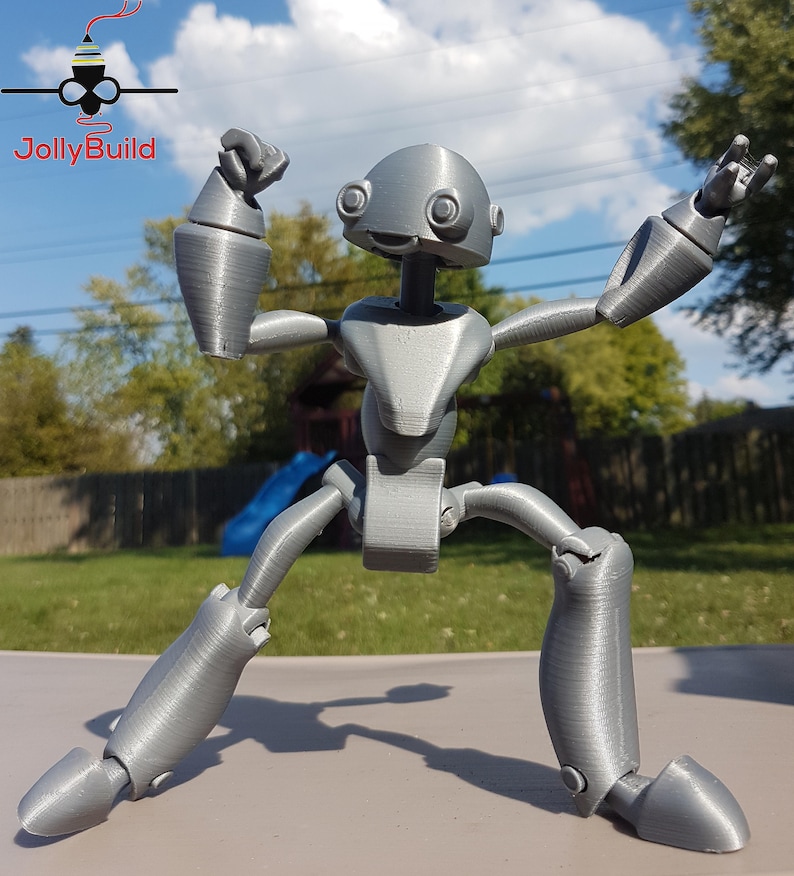 May include: A gray, articulated robot figure with a large head and large eyes. The robot is posed with its arms raised and its legs spread apart.