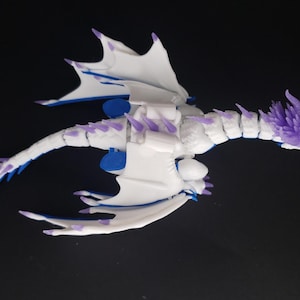 May include: A white and blue dragon figurine with purple accents. The dragon has large wings, a long tail, and a detailed head. The figurine is made of plastic and is set against a black background.
