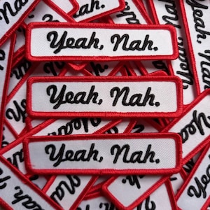 Puede incluir: Primer plano de varios parches de tela blanca con bordes rojos. Los parches tienen el texto "Yeah, Nah." bordado en letra cursiva negra.