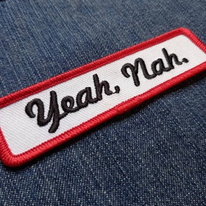 Puede incluir: Parche blanco bordado con costuras rojas alrededor de los bordes. El parche dice "Yeah, Nah." en letras cursivas negras.