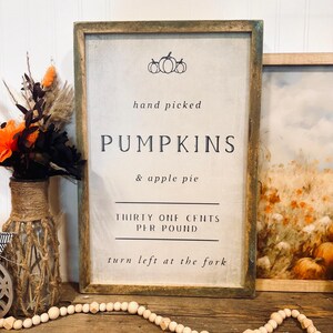May include: A rustic wooden sign with the text "hand picked PUMPKINS & apple pie THIRTY ONE CENTS PER POUND turn left at the fork". The sign is decorated with a small image of pumpkins.