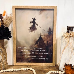 May include: A framed print featuring a witch flying over rooftops, with the text "When the world is wrapped in slumber and the moon is sailing high. If you peep between the curtains, you'll see witches riding by." The artwork has a vintage, Halloween theme.