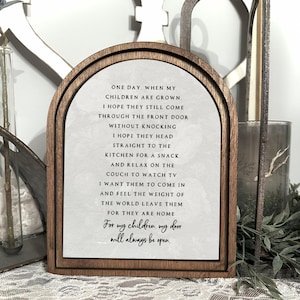 Puede incluir: Letrero enmarcado en madera con una parte superior arqueada. El letrero tiene un fondo blanco con texto negro que dice: "Un día, cuando mis hijos sean mayores... Para mis hijos, mi puerta siempre estará abierta."