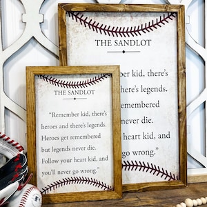 May include: Two framed prints with a baseball theme. The top print has the text "THE SANDLOT" and a red baseball stitch design. The bottom print has the text "THE SANDLOT" and a quote from the movie: "Remember kid, there's heroes and there's legends. Heroes get remembered but legends never die. Follow your heart kid, and you'll never go wrong."
